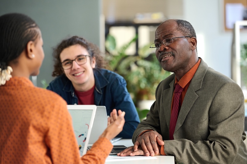 Boomers in the Workforce. Portrait of smiling senior man discussing ideas in business meeting with young colleagues in office copy space