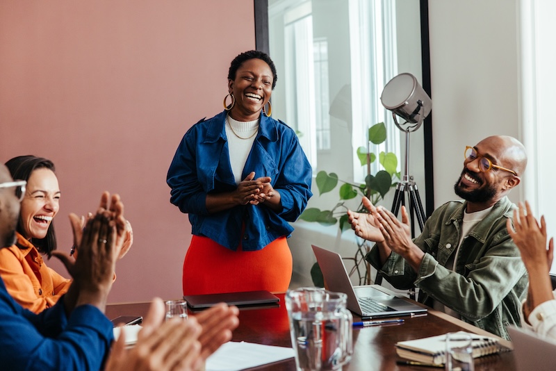Boomers in the Workforce. Group of colleagues in conference room applauding a team member. Celebration of achievement and collaboration. Corporate teamwork and accomplishment marked by warm praise.